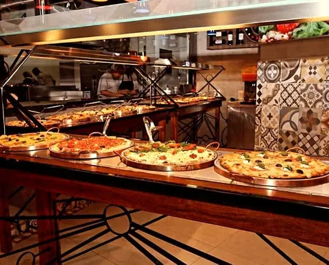 O balcão do buffet com as pizzas nas bandejas de cobre e o pizzaiolo ao fundo