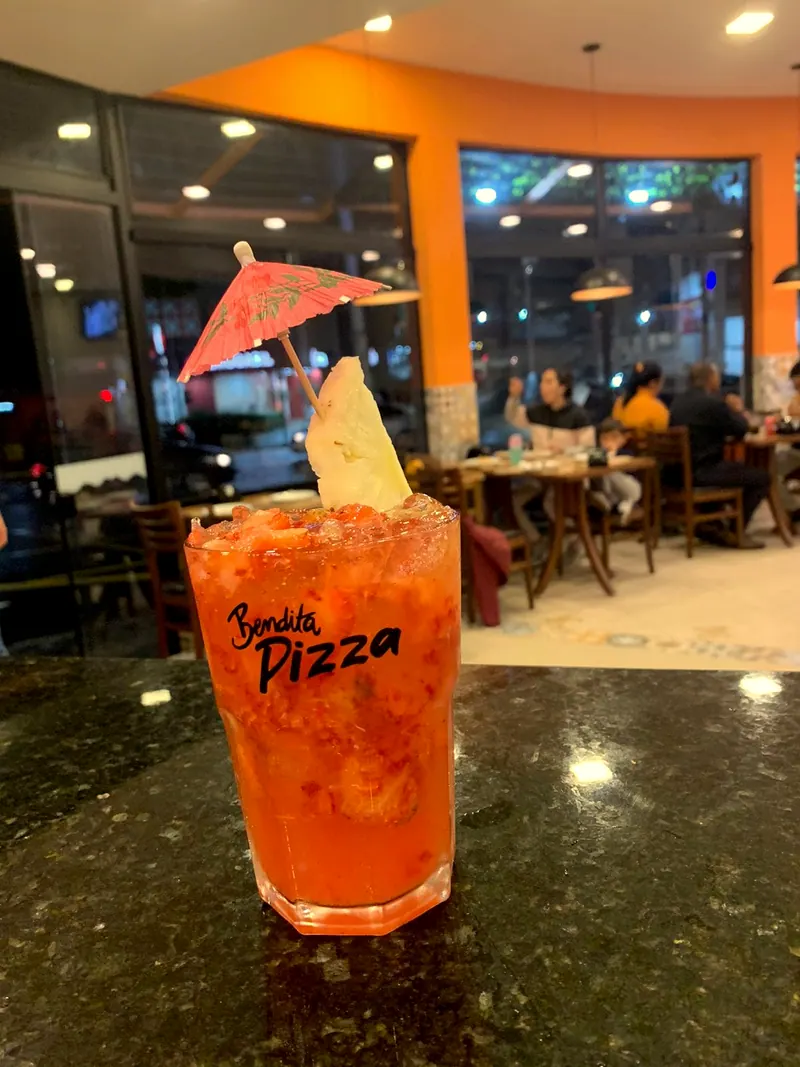 Drink vermelho com guarda-chuvinha no copo da Bendita Pizza, no salão à noite