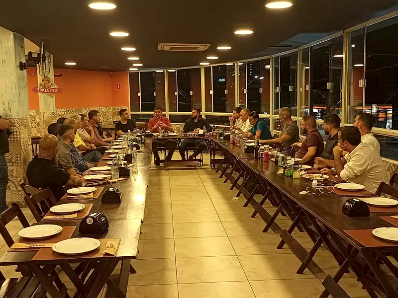 Um grupo grande reunido nas mesas longas do salão, em U