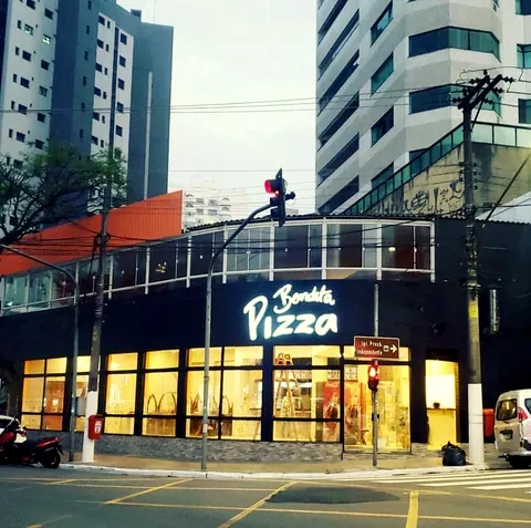 A fachada da Bendita Pizza na esquina, com o letreiro aceso