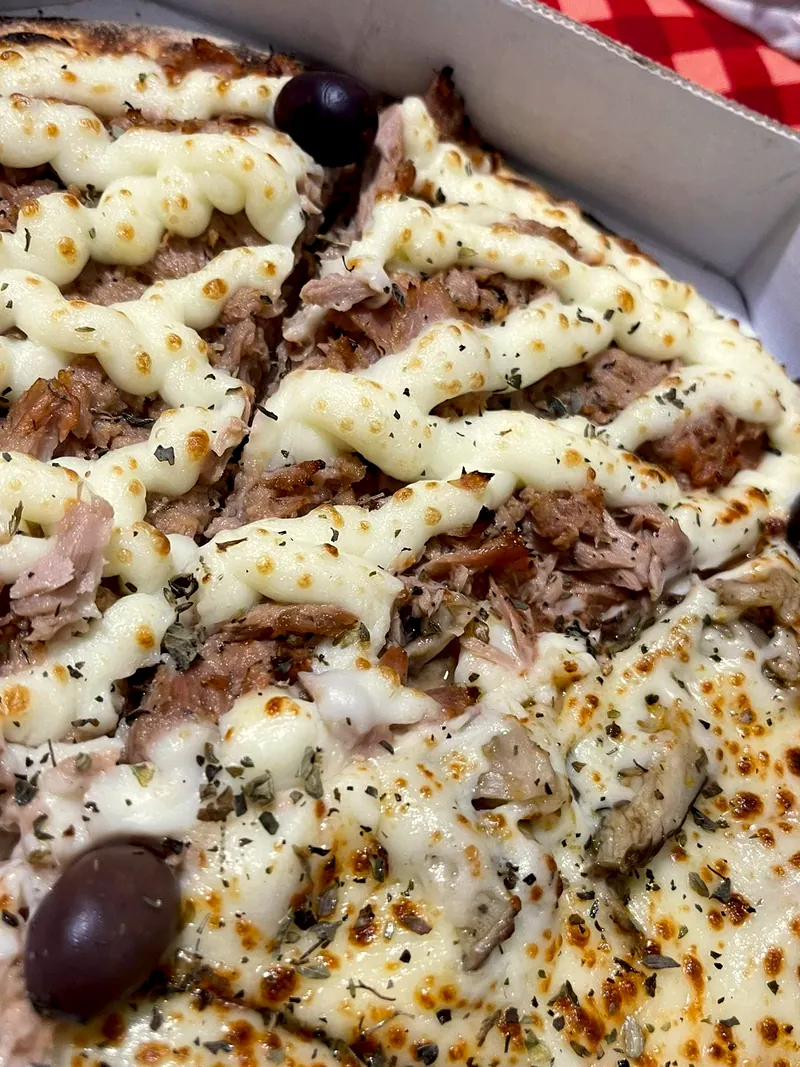Pizza de perto, com cream cheese em fios, carne desfiada, orégano e azeitonas pretas