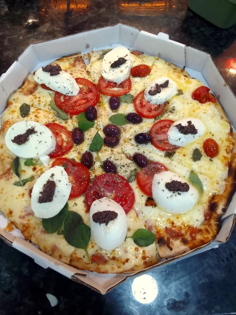 Pizza vista de cima com rodelas de tomate, muçarela, manjericão e azeitonas pretas