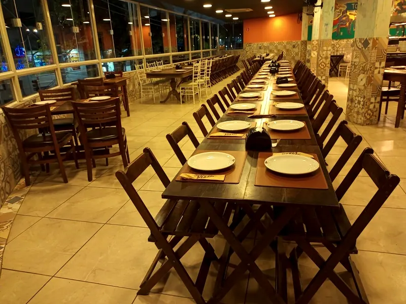 O salão montado para um evento, com a mesa longa posta, as paredes de vidro e a parede laranja